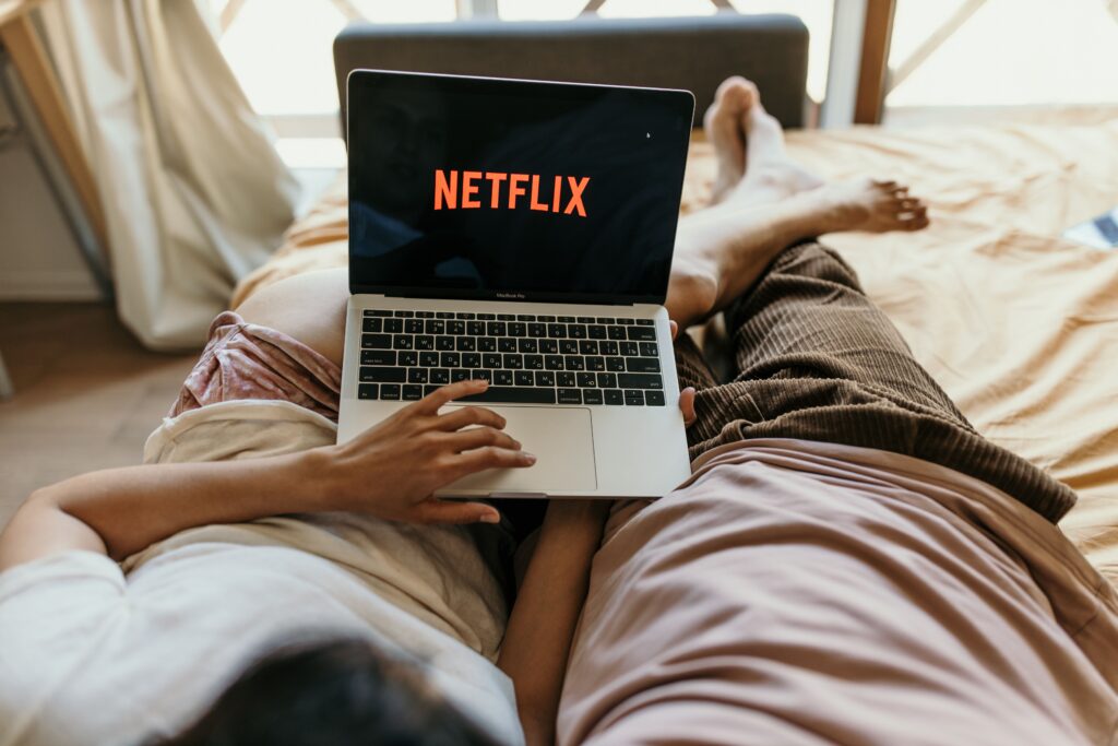 Persona viendo acciones Netflix en un portátil desde la cama.